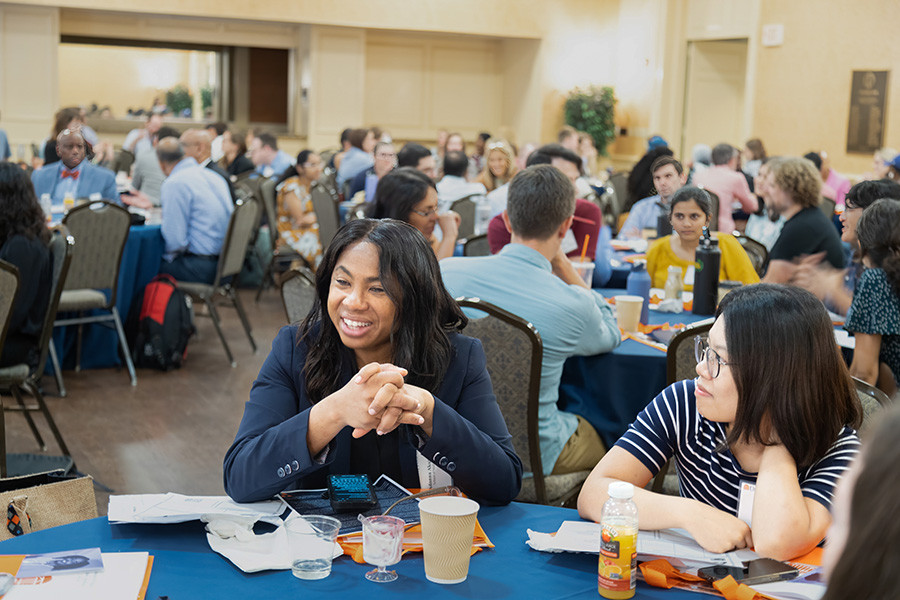 A large group of workshop participants sitting at tables interacting with each other.