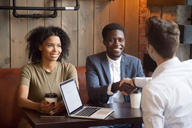 Three adults - two men and a woman meet at a table over coffee.