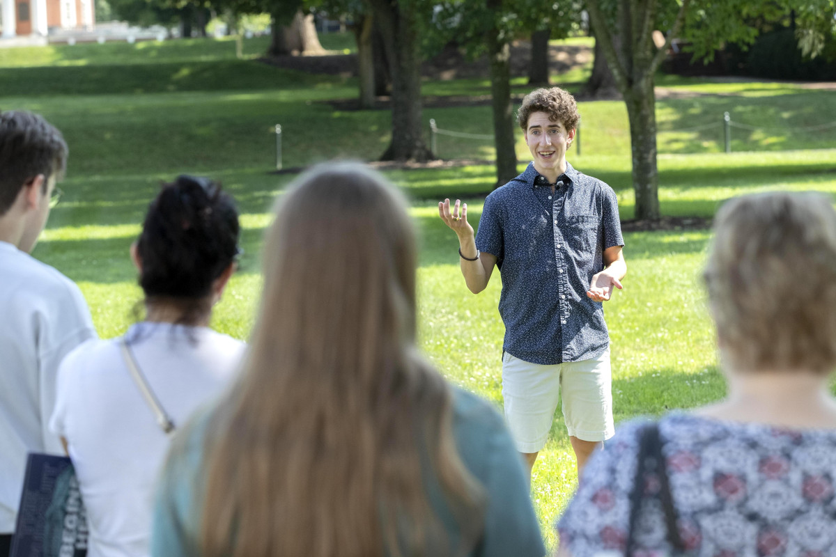 A young man speaking in front of a small crowd on the UVA Grounds.