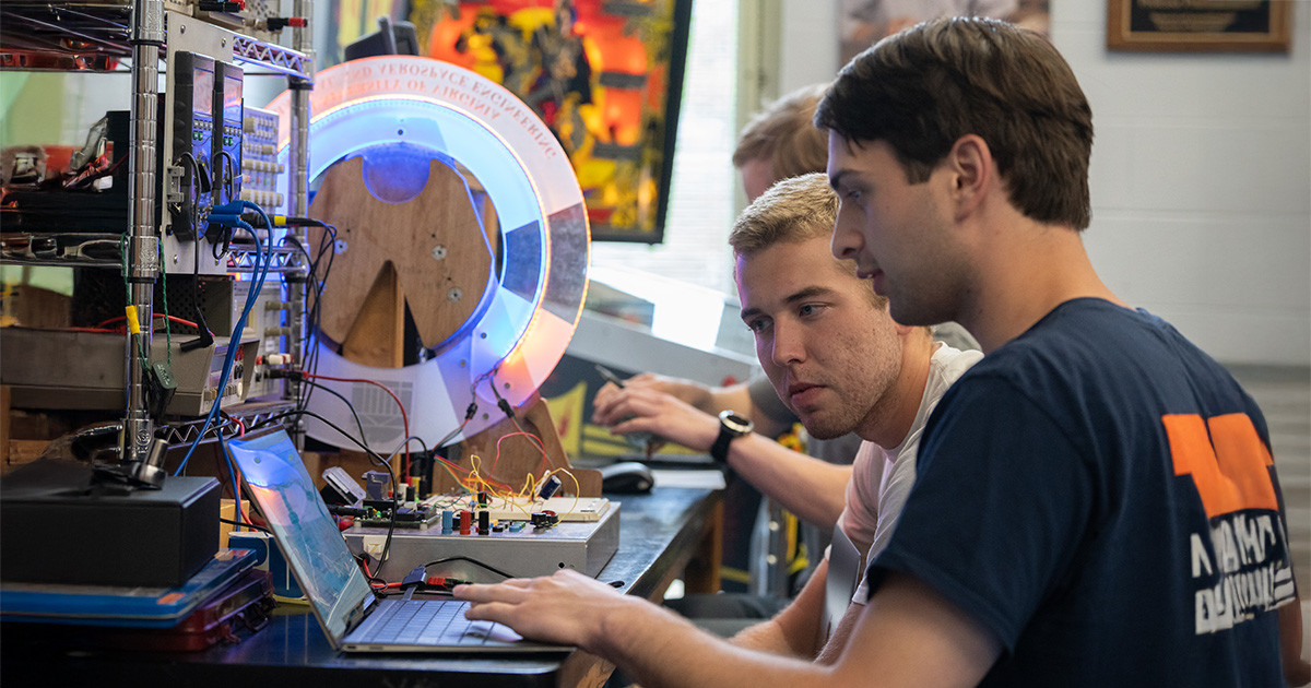 A team of three students workin in a lab with computers and electrical equipment.