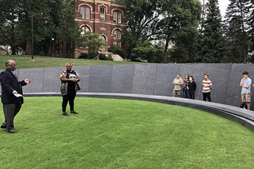 A group of adults and adolescents stand at the Memorial for Enslaved laborers on UVA grounds