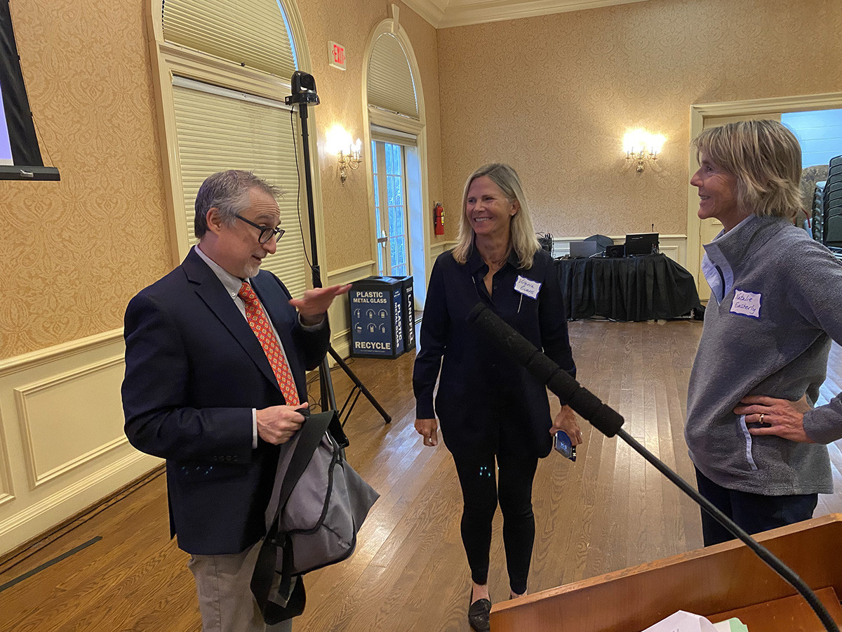 Professor Paul Freeman, standing near a podium, chats with two RFA members after a lecture.