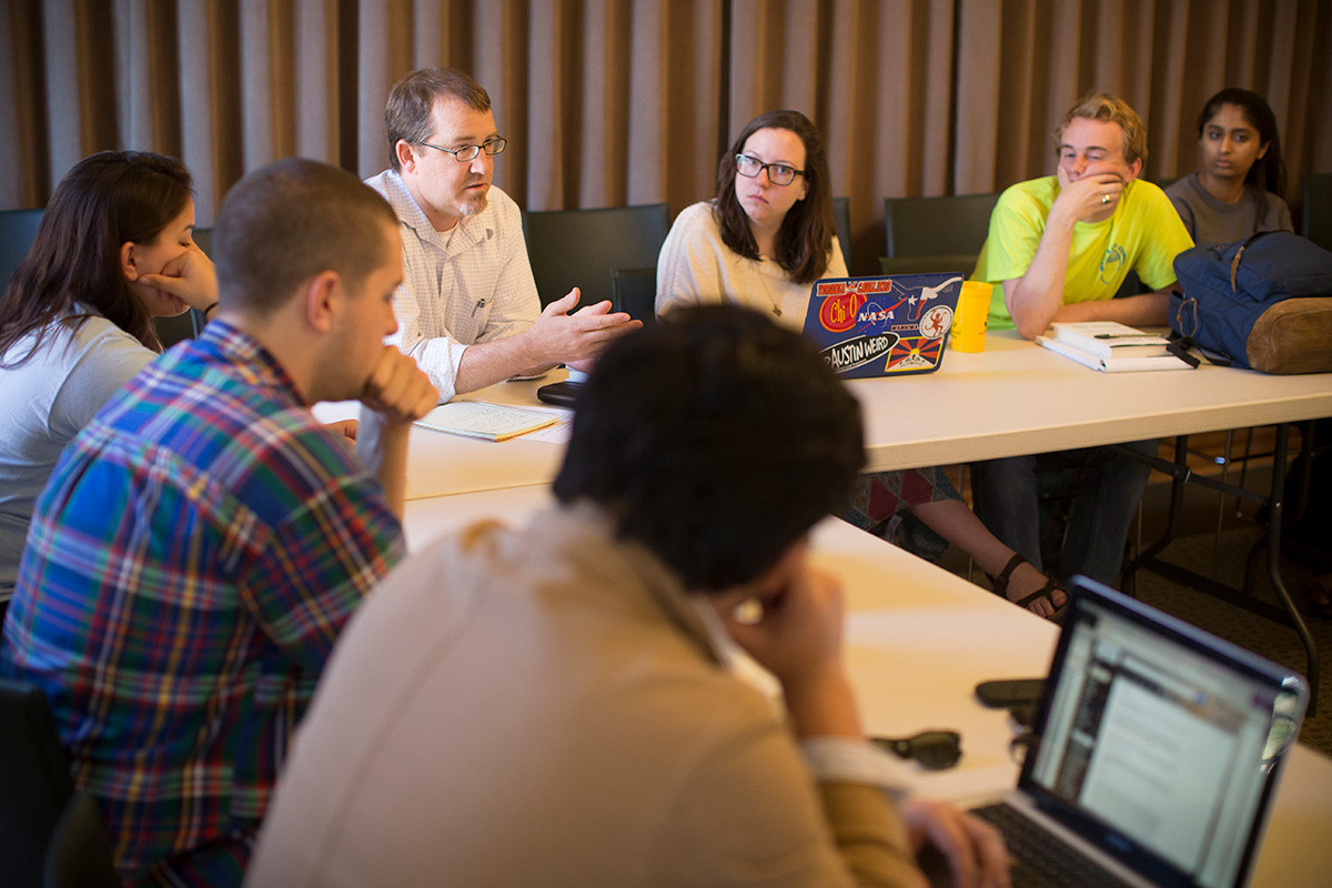 Professor talking to students while sitting around a table.