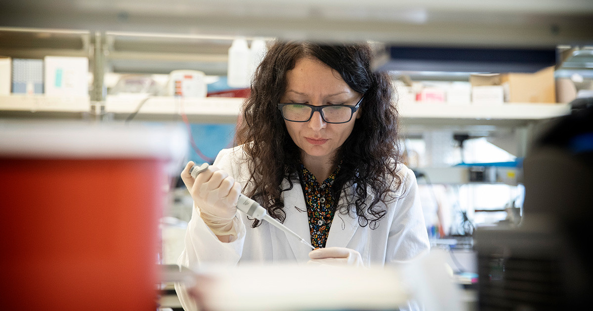 A researcher wearing a white coat fills a tube using a syringe.