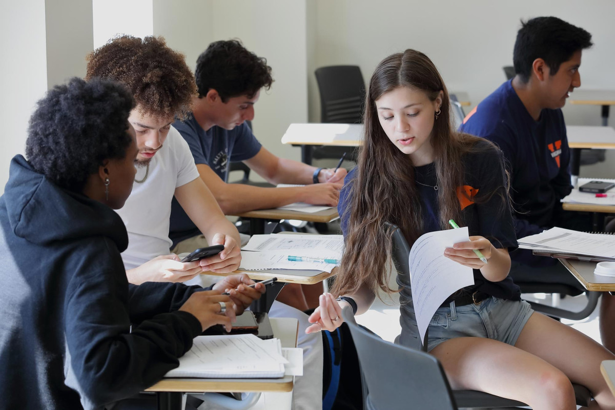 Three students seated at classroom desks reviewing paper printouts