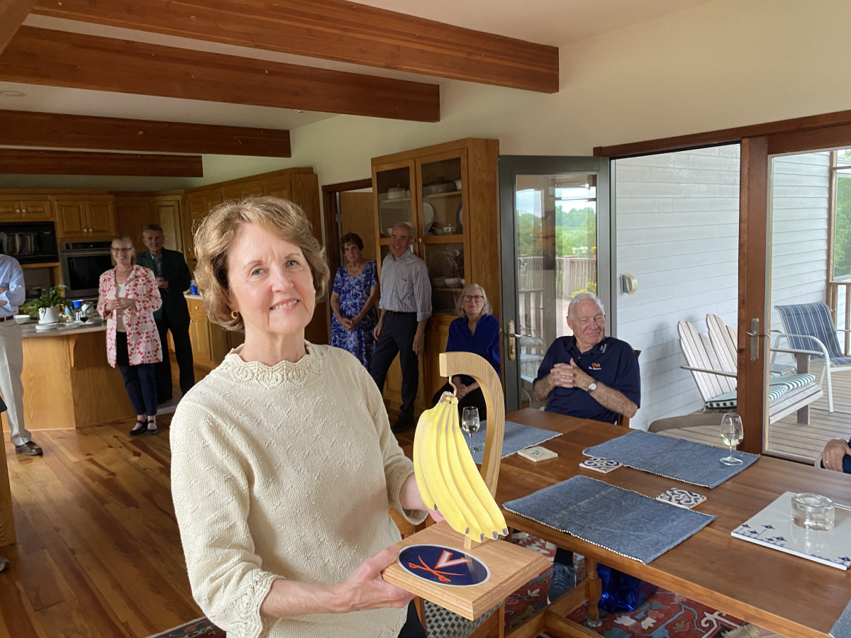 Kathy Thornton standing in a dining room holding a banana hanger with the UVA Cavalier's emblem on it.