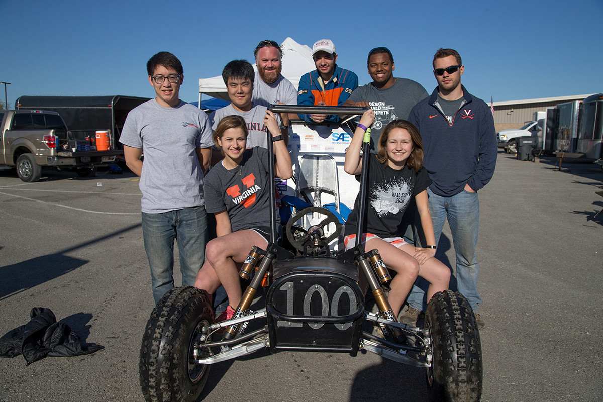 A diverse group of students sitting on and standing around a dune buggy.