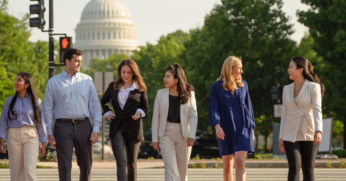 A diverse group of young professionals walk in front of the US Capitol building.