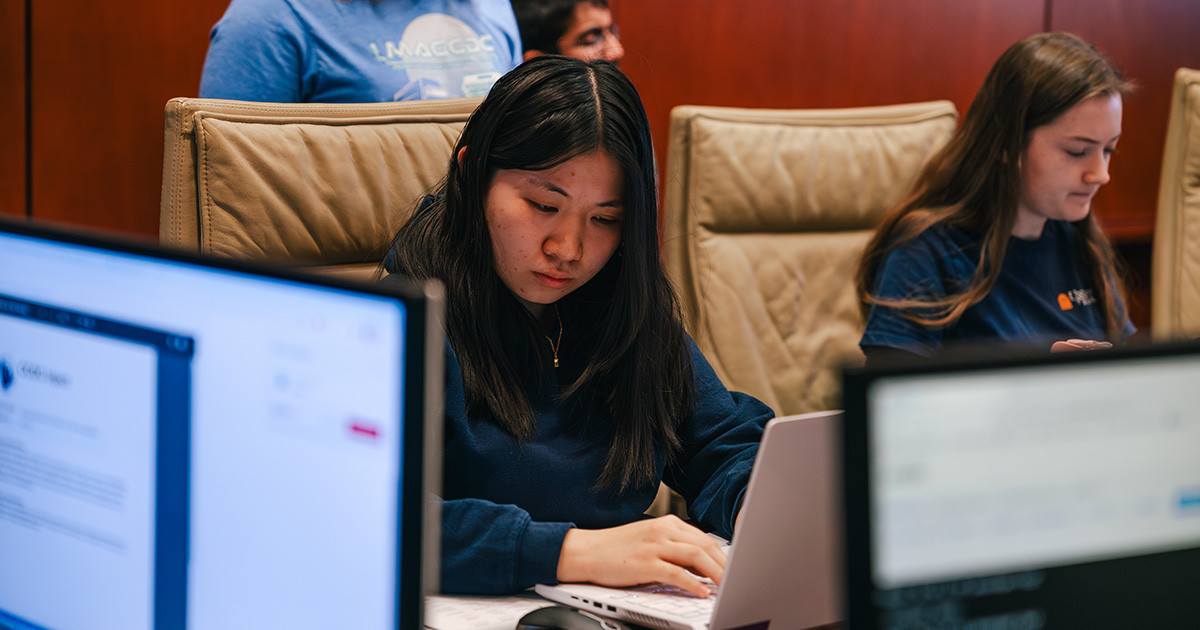 Two female student sitting at a table, writing on their laptop.