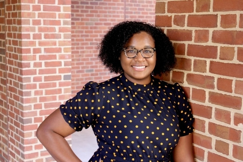 Headshot of Jessica Forrester standing next to brick wall, facing camera, and smiling