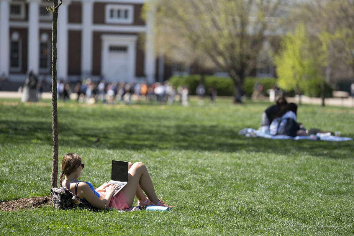 student with laptop leaning against tree on the lawn