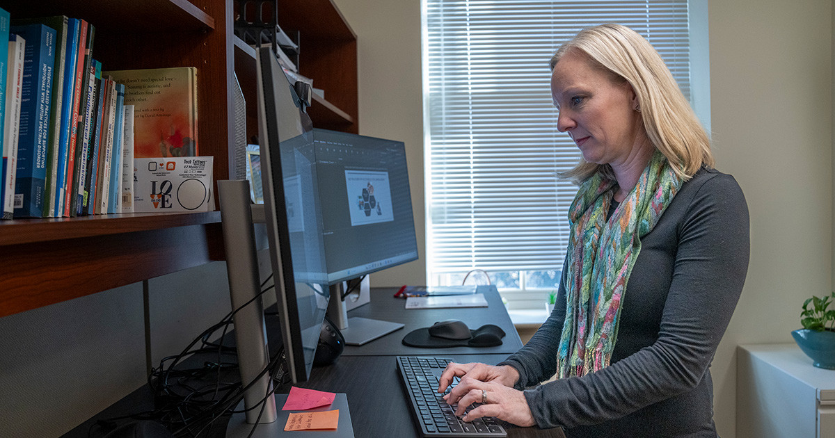 Professor stands at a high desk while looking at a computer monitor.