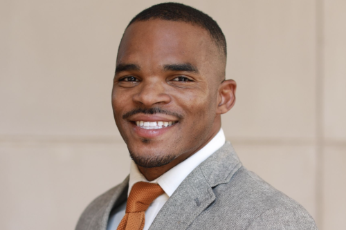 Headshot of a smiling man dressed in a jacket and tie.