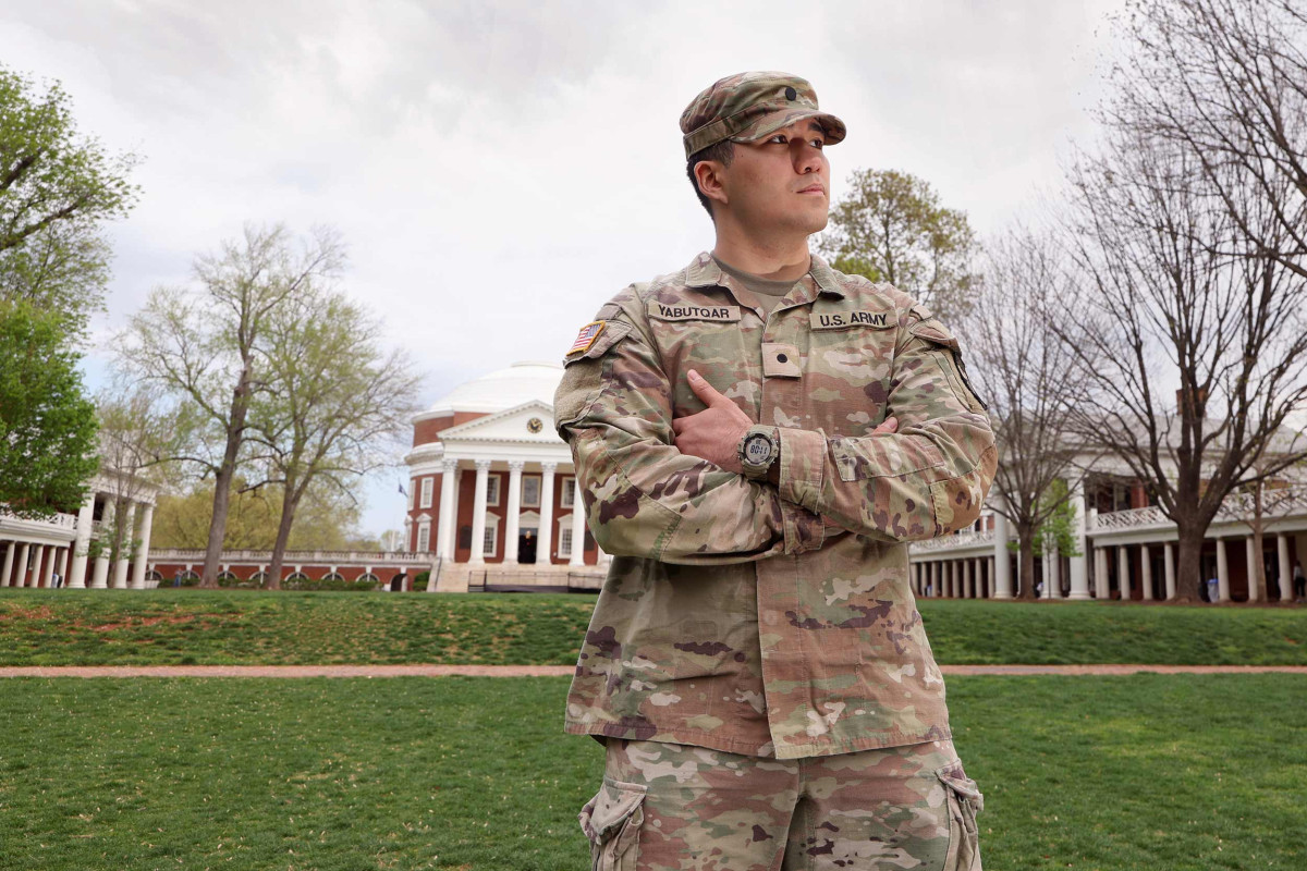 A male ROTC student dressed in Army fatigues stands with arms crossed while on the UVA Lawn.
